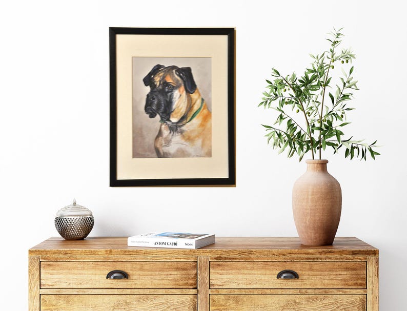 May include: A framed painting of a brown and black dog with a green collar. The dog is looking to the left of the frame. The painting is in a black frame and is hanging on a white wall.