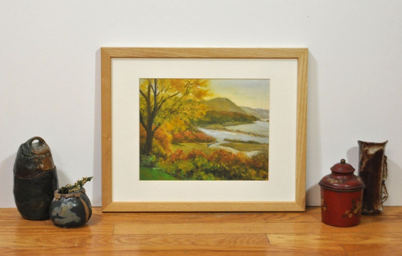 Puede incluir: Pintura enmarcada de una escena de paisaje con un r&iacute;o serpenteando por un valle con follaje oto&ntilde;al. La pintura est&aacute; en un marco de madera claro.