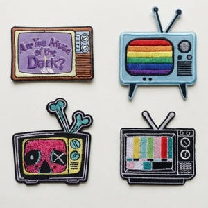 May include: Four embroidered patches shaped like vintage television sets. One displays the text Are You Afraid of the Dark? in purple. Another features a rainbow screen. A third shows a pink skull with bones, and the last displays colour bars.