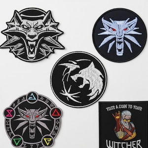 May include: A collection of black and white embroidered patches featuring the wolf emblem from The Witcher series. The patches include various designs of the wolf head, with some featuring the Witcher medallion and text.