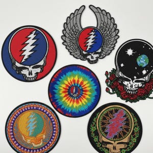 May include: A collection of seven embroidered patches featuring skull designs. The patches showcase a variety of colors, including red, blue, yellow, and green, with intricate details and patterns. Some patches have wings, tie-dye, and floral elements.