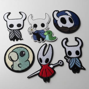 May include: A collection of seven embroidered patches featuring various cartoon characters. The patches showcase a white character with large eyes and a horned head, in different poses and with various accessories. The color palette includes white, black, blue, red, and green.