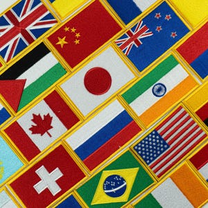 May include: A collection of embroidered patches featuring various national flags, including the United States, Canada, and Japan. Each patch has a gold border and showcases the flag's colors and designs. The flags are arranged in a diagonal pattern.