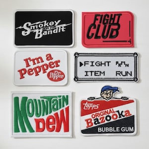 May include: A collection of embroidered patches with various designs and text. The patches include the phrases "Smokey and the Bandit", "Fight Club", "I'm a Pepper Dr. Pepper", "Fight PKMN Item Run", "Mountain Dew", and "Topps Original Bazooka Bubble Gum".