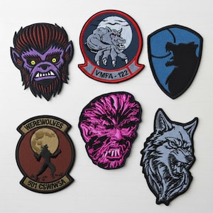 May include: A collection of embroidered patches featuring werewolf designs. The patches showcase various werewolf faces and silhouettes, with colors including purple, red, blue, and black. Some patches include text such as "Werewolves" and "VMFA-122".