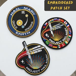 May include: Embroidered patch set featuring three unique designs. One patch is circular with text and a graphic, another features a rocket design with flags, and the third has a rocket design with the text "Project Hail Mary".