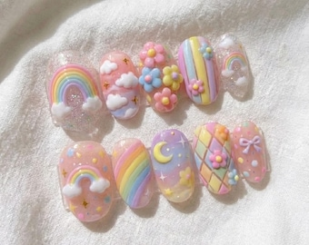 May include: A set of ten artificial nails with a pastel rainbow, cloud, flower, and moon design. The nails are oval-shaped and feature a variety of colors, including pink, blue, yellow, and purple. Some nails have glitter accents.