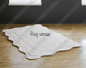 May include: A cream-coloured, organically shaped rug with a wavy pattern and a light brown trim. The rug is placed on a wooden floor, with the text "Rug venue" displayed. This is a decorative floor covering, suitable for a living space.