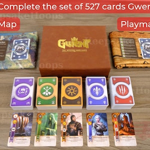 Może przedstawiać: Zestaw do gry w karty Gwent z brązowym pudełkiem ze złotymi literami, dwoma matami do gry i kilkoma stosami kart. U góry widoczny jest tekst "Complete the set of 527 cards Gwent". Maty do gry są oznaczone jako "Map" i "Playmat".