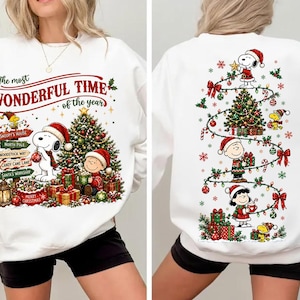 Może przedstawiać: Biała bluza z okrągłym dekoltem i świąteczną grafiką z postaciami Peanuts. Z przodu widoczny jest Snoopy, Charlie Brown, choinka oraz napis The most WONDERFUL TIME of the year. Z tyłu znajduje się Snoopy, Charlie Brown i Lucy dekorujący drzewko.