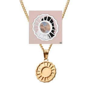 Op de afbeelding: Een goudkleurige ketting met een hanger met een sunburst-ontwerp. De ketting is een schakelstijl. De hanger is rond met een centrale cirkel en stralende lijnen. Een vierkante afbeelding met een witte lijst en een wolkenlandschap is ook zichtbaar.