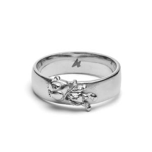 Op de afbeelding: Een zilveren ring met een gedetailleerd eekhoornontwerp. De ring heeft een brede band en een kleine, gestileerde eekhoornfiguur aan de voorkant. Een klein symbool is gegraveerd op het oppervlak van de ring.