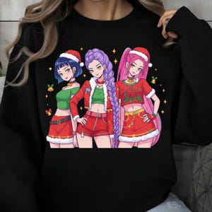 May include: Black crew neck sweatshirt with a Christmas anime graphic. The graphic shows three anime characters in Santa hats and red outfits. The characters have blue, purple, and pink hair. Gold stars and bells are also in the graphic.