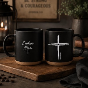 Puede incluir: Dos tazas de cerámica negras con base de color natural. Una taza tiene los nombres "Sophia" y "Alex" con una cruz. La otra taza presenta una cruz blanca y el texto "FATHERHOOD IS KINGDOM WORK" y "PROVERBIOS 22:6".