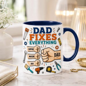 Puede incluir: Taza de cerámica blanca con interior y asa azules. La taza presenta el texto "DAD FIXES EVERYTHING" con ilustraciones de herramientas y nombres. El diseño incluye un puño con la palabra "DAD" tatuada.