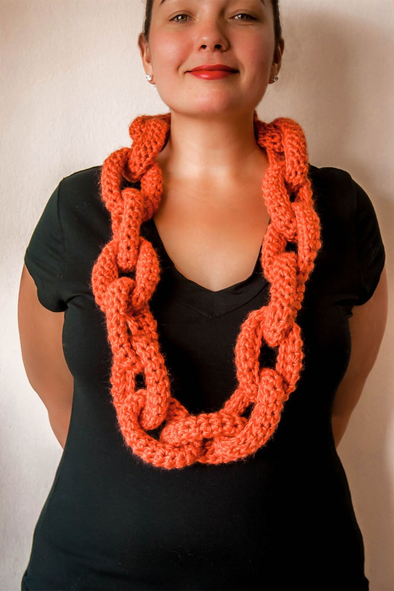 May include: A woman wearing a black top with a bright orange crocheted chain link necklace.