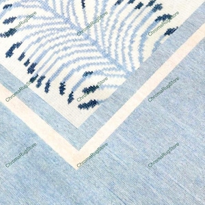 May include: A section of a rug with a blue and white leaf pattern. The rug has a light blue border and a white stripe. The leaf pattern is in shades of blue and white.