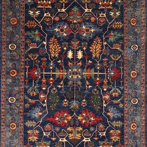 May include: A rectangular, intricately patterned rug with a deep blue field. The design features a central medallion and repeating floral and geometric motifs in red, orange, green, and cream. A detailed border frames the rug, adding to its ornate appearance.