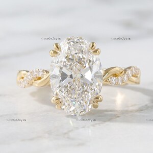 Peut inclure: Une bague en or avec une grande pierre centrale transparente de taille ovale maintenue par huit griffes. L'anneau présente un design torsadé des deux côtés, orné de petites pierres rondes et transparentes incrustées sur le métal.