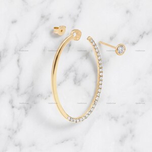 May include: A gold hoop earring featuring a row of small clear stones along the outer edge, accompanied by a separate gold post earring with a single round clear stone, and a small gold earring back piece, all displayed as individual components.