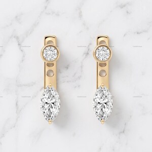 Puede incluir: Un par de pendientes de oro con un diseño de barra vertical. Cada pendiente tiene una piedra clara redonda de talla brillante en la parte superior y una piedra clara de talla marquesa en la parte inferior, unidas por una barra dorada con dos aberturas circulares.
