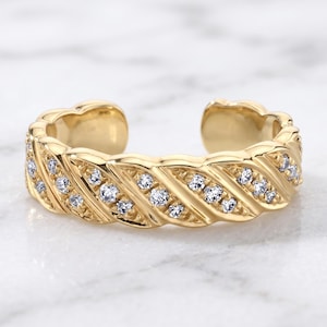 Puede incluir: Un anillo abierto de oro con un diseño texturizado de nervaduras diagonales. La banda está acentuada con una serie de pequeñas piedras claras de corte redondo incrustadas en las ranuras, creando un efecto brillante en la superficie.