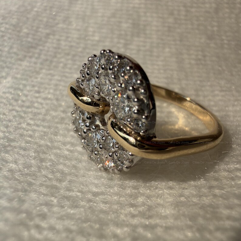 May include: A gold ring with a cluster of small, clear gemstones set in a circular design. The ring has a gold band and a gold accent that wraps around the gemstone cluster.
