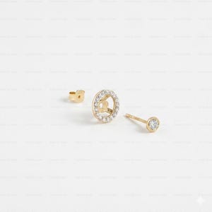 May include: Gold-toned stud earrings with a diamond-encrusted circular design and a single diamond stud. The earrings are displayed with a matching earring back. The jewelry is set against a white background.