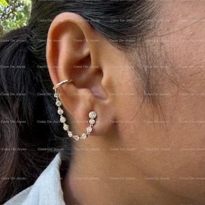 May include: A gold ear cuff and earring set. The ear cuff wraps around the upper ear, connected by a delicate chain of small, sparkling stones to a stud earring. The jewelry is designed to be worn on one ear.