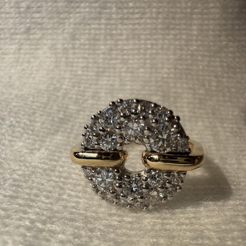 May include: A diamond ring with a circular design. The ring features a gold band with a cluster of small diamonds around the outer edge. The center of the ring is open, creating a unique and elegant look.