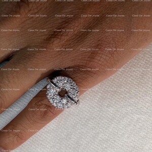May include: A silver ring featuring a circular design encrusted with numerous small, sparkling gemstones. The ring has a unique, open center and is worn on a finger. The ring is a piece of jewelry.