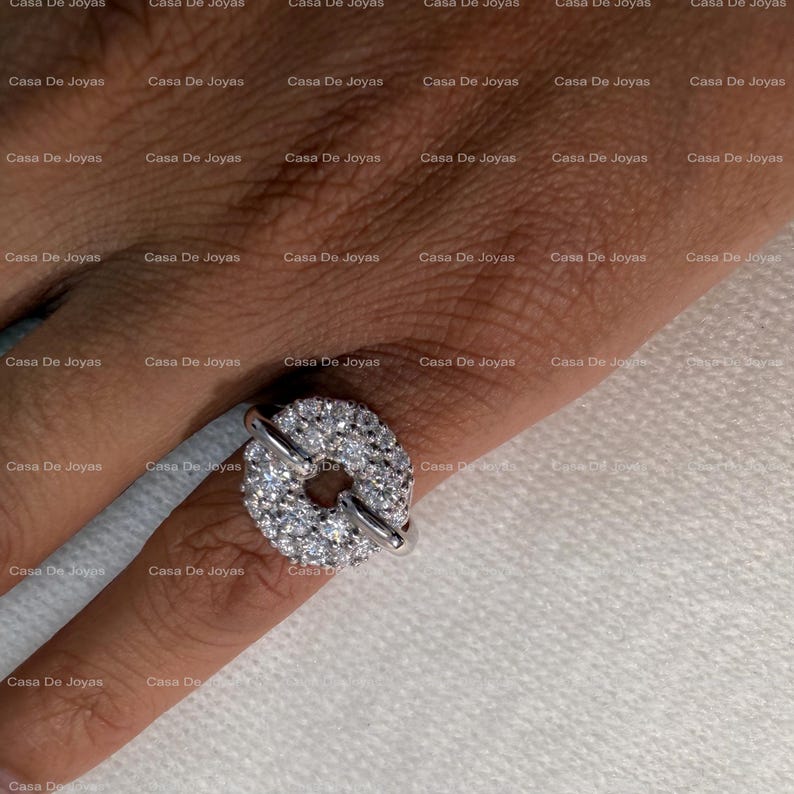 May include: A silver ring featuring a circular design encrusted with numerous small, sparkling gemstones. The ring has a unique, open center and is worn on a finger. The ring is a piece of jewelry.