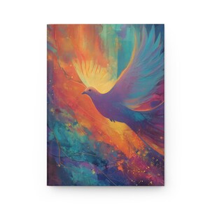 Op de afbeelding: Een notitieboek met een levendig, abstract schilderij van een vliegende duif. Het kunstwerk heeft een palet van warme kleuren zoals oranje en geel, gecontrasteerd met koele blauw- en paarse tinten. De duif is het middelpunt, met wijd gespreide vleugels.