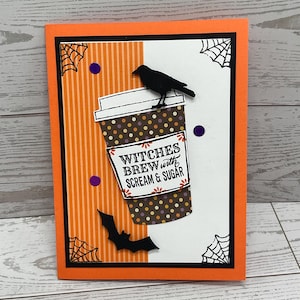 May include: Halloween greeting card with an orange and black border. The card features a coffee cup design with the text "Witches Brew with Scream & Sugar." A black crow and bat are also included, along with spiderwebs and purple dots.