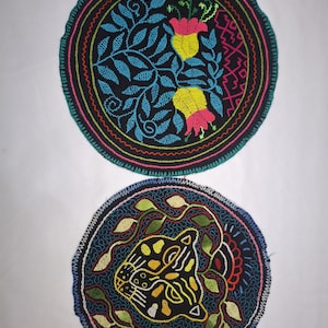 Könnte beinhalten: Zwei runde, gestickte Aufnäher. Einer zeigt blaue Blätter und gelbe und rosa Blüten auf schwarzem Grund. Der andere Aufnäher hat ein Tigergesicht mit gelben und schwarzen Details auf dunkelblauem Grund.