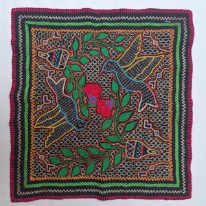 May include: Square textile with a black background featuring a detailed embroidered design. The design includes two hummingbirds, red flowers, green leaves, and decorative elements. The border is a combination of colors including red, green, and black.