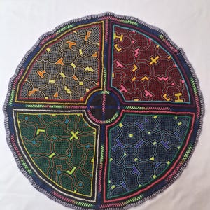 Könnte beinhalten: Ein rundes, mehrfarbiges Textil mit einem segmentierten Design. Das Textil ist in vier Abschnitte unterteilt, jeder mit einem einzigartigen Muster und Farbschema, darunter Schwarz, Rot, Grün und Blau. Die Kanten sind mit einer dekorativen Naht versehen.