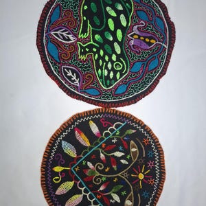 Könnte beinhalten: Zwei runde, schwarz gestickte Aufnäher mit farbenfrohen Designs. Einer zeigt ein grünes und schwarzes Wesen mit floralem Rand. Der andere hat ein florales und geometrisches Design mit orangefarbenen, gelben und blauen Akzenten. Beide haben einen Zickzack-Rand.