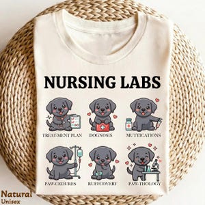 May include: Cream-colored unisex t-shirt featuring the text "NURSING LABS" above six cartoon Labrador puppies. Each puppy illustrates a different medical procedure, such as "TREAT-MENT PLAN" and "PAW-THOLOGY". The shirt also has the words "Natural Unisex" printed on it.