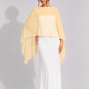 May include: A sheer, pale yellow chiffon capelet with a boat neckline and flowing, asymmetrical hemline, worn over a floor-length, strapless white column dress. The capelet features a lightweight, translucent fabric that drapes over the shoulders.