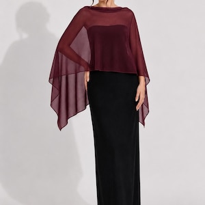 May include: A floor-length black column dress featuring a strapless bodice and a sheer, burgundy-colored chiffon capelet overlay that drapes over the shoulders and arms, creating a layered silhouette with a straight hemline and minimalist design.