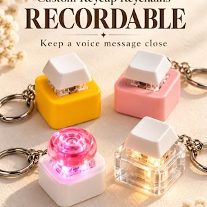 以下が含まれることがあります： 金属リング付きのキーキャップ型キーホルダー4個。テキスト：Custom Keycap Keychains RECORDABLE Keep a voice message close。黄色、ピンク、ピンクの丸いボタンが付いた白、内部にライトが光る透明なキーホルダーがそれぞれ1つずつあります。
