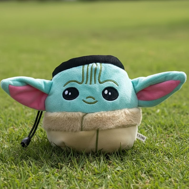 Peut inclure: Un sac &agrave; magn&eacute;sie en peluche en forme de personnage de couleur sarcelle, avec de grands yeux noirs, des oreilles doubl&eacute;es de rose et un cordon de serrage noir. Le sac a un fond de couleur beige et un dessus noir, ressemblant &agrave; un personnage populaire.