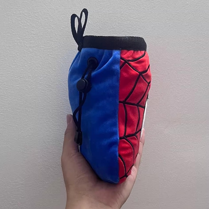 Peut inclure: Sac &agrave; magn&eacute;sie d'escalade bleu et rouge avec fermeture &agrave; cordon. Le sac est divis&eacute; en deux, avec un mat&eacute;riau bleu semblable &agrave; du velours d'un c&ocirc;t&eacute; et un motif de toile d'araign&eacute;e rouge de l'autre. Cordon et boucle noirs.