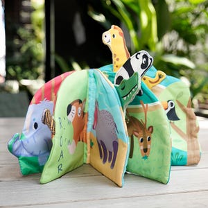 Könnte beinhalten: Ein farbenfrohes Stoffbuch für Babys mit verschiedenen Dschungeltieren. Das Buch hat Seiten mit Illustrationen eines Elefanten, Hundes, Nashorns, Hirsches und Tukan. Das Cover zeigt eine Giraffe, einen Panda und ein Alligator. Das Wort "ROAR" ist auf einer Seite aufgedruckt.