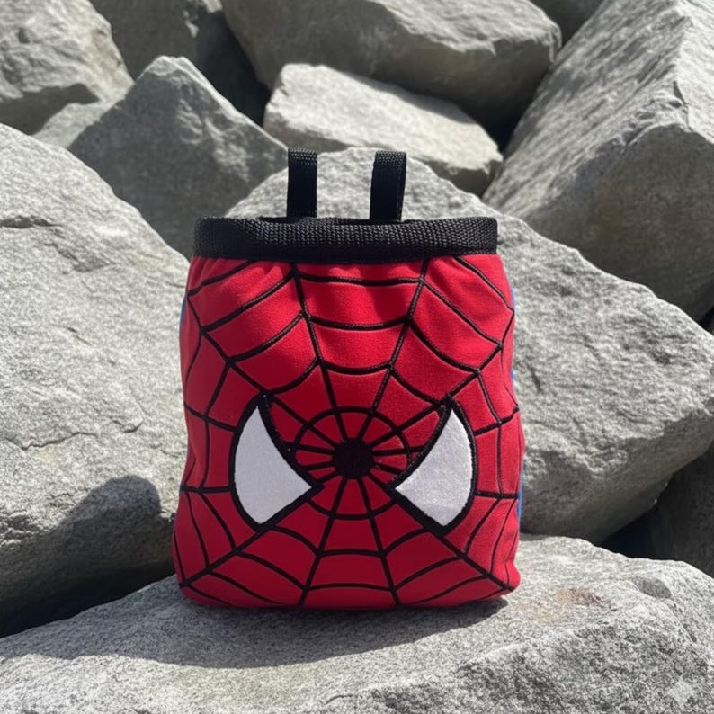 Peut inclure: Sac &agrave; magn&eacute;sie rouge avec un bord noir et deux boucles noires. Le sac pr&eacute;sente un motif Spider-Man avec un motif de toile d'araign&eacute;e rouge et des formes d'yeux blancs. Con&ccedil;u pour l'escalade.