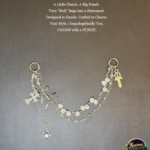 Könnte beinhalten: Silberner Taschenanhänger mit mehreren Ketten, Kreuzen und einem Herzanhänger. Der Anhänger enthält einen goldfarbenen Schlüssel und einen Ring zum Befestigen. Der Text auf dem Bild lautet "A Little Charm. A Big Punch."