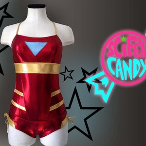 Puede incluir: Traje de baño rojo y dorado con un diseño triangular azul en el pecho. El traje de baño tiene un top halter y una pierna de corte alto.