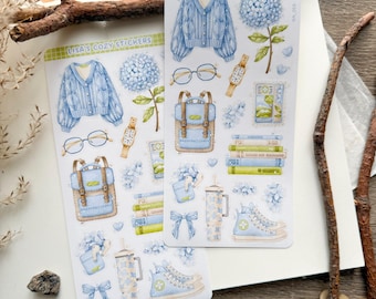 May include: Two sticker sheets with watercolor illustrations. The stickers feature a blue cable knit sweater, backpack, glasses, watch, books, sneakers, and other cozy-themed designs. The text "LISA'S COZY STICKERS" is at the top of each sheet.