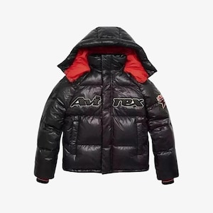 Puede incluir: Chaqueta acolchada negra con capucha y forro rojo. La chaqueta presenta el texto "Avi rex" en letras blancas y negras en el pecho. Un peque&ntilde;o parche es visible en la manga derecha. La chaqueta tiene un acabado brillante.